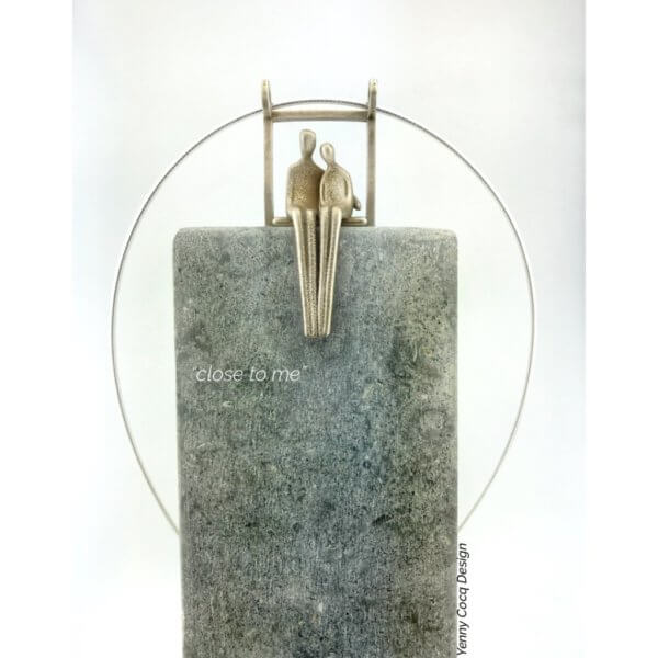 Pendant of couple seated in embrace sits atop a stone