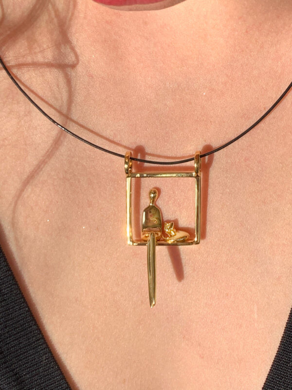 Close up on model's chest of gold pendant of woman seated next to cat.