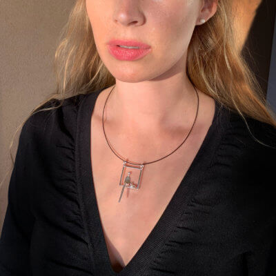 Model wearing necklace. Silver pendant shows person sitting next to cat